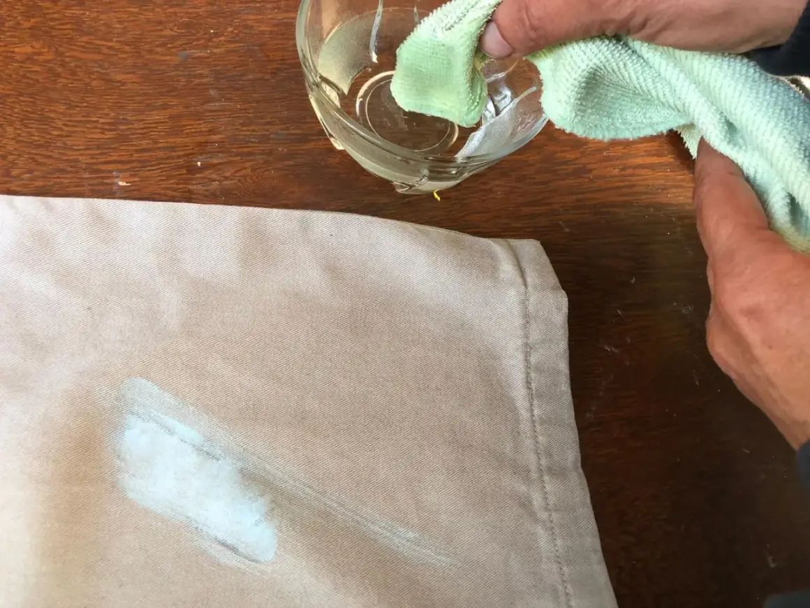 Mani che tamponano una macchia di vernice secca su un tessuto beige con un panno umido, per togliere macchie di vernice secca dai vestiti.