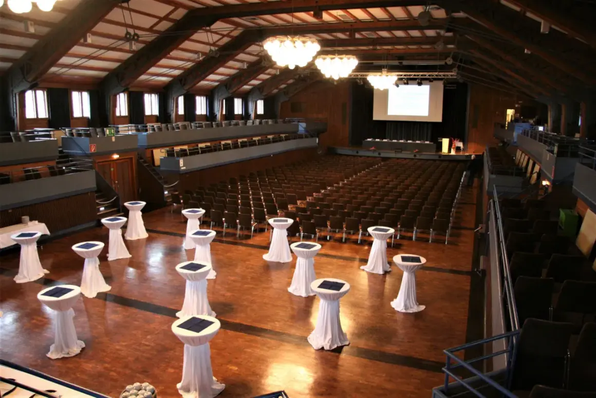 Innenansicht der Stadthalle Herrenberg mit vielen Sitzreihen, einer Bühne und Stehtischen, bereit für eine Veranstaltung.