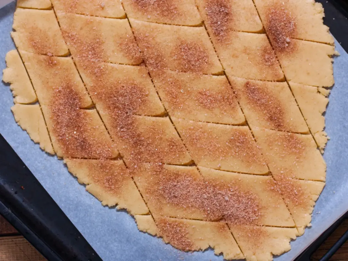 Surowe ciasto na ciasteczka pokrojone w romby, posypane cukrem z cynamonem.