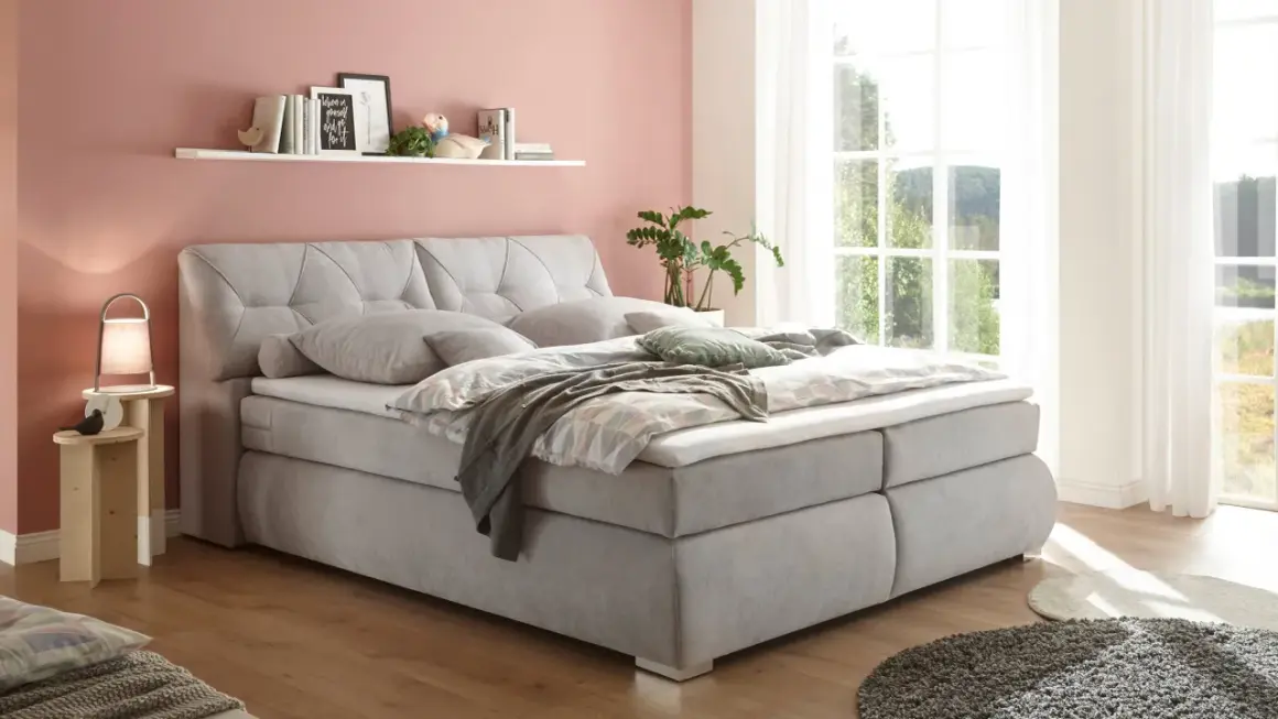 Einladendes, graues Boxspringbett mit gestepptem Kopfteil, das Ruhe und Harmonie ausstrahlt – perfekt für ein Feng Shui Bett.