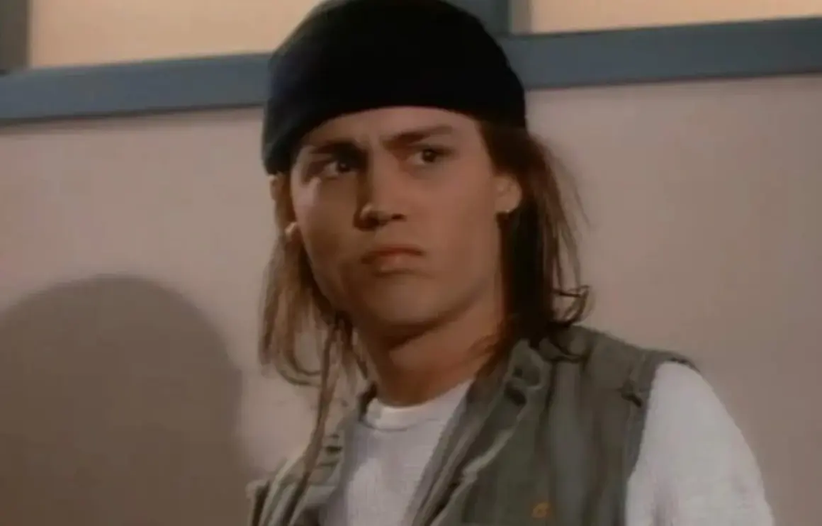 Johnny Depp ung med långt hår och svart mössa, bär en väst över en vit tröja.