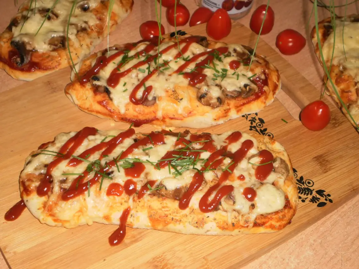 Dwa podłużne, zapieczone ciasta na pizzę z serem, pieczarkami i keczupem, ozdobione szczypiorkiem.