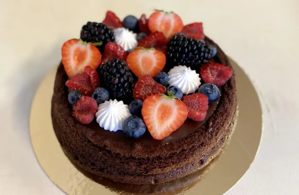 En mörk chokladtårta med ganache, toppad med färska bär och maränger. En festlig chokladtårta med ganache som ser utsökt ut.