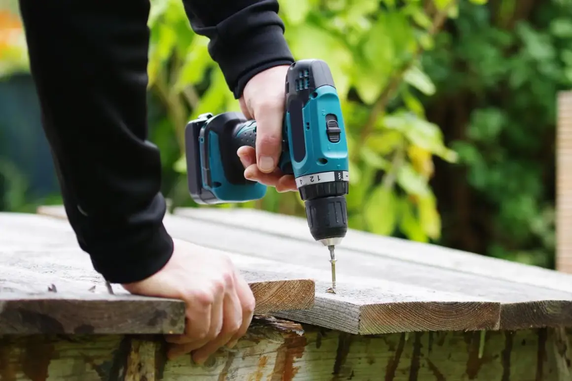 Main tenant une perceuse sans fil, il visse une planche de bois. La puissance perceuse permet de réaliser des travaux de bricolage facilement.