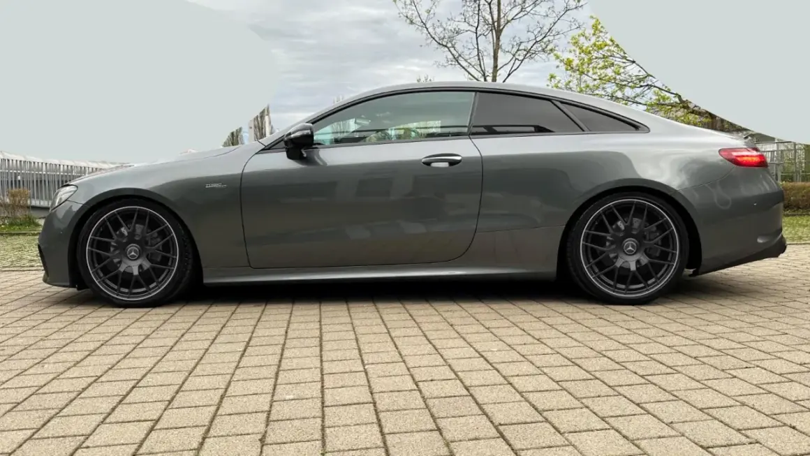 Szary Mercedes-AMG E53 coupe z przyciemnianymi szybami i czarnymi felgami stoi na kostce brukowej.