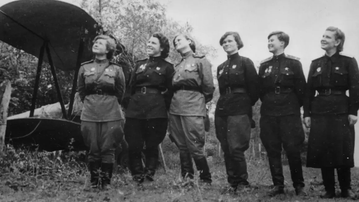 Seis mujeres con uniformes militares posan junto a un biplano. Son las brujas de la noche, listas para volar.