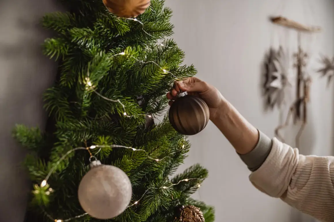 Eine Hand schmückt einen Wand-Weihnachtsbaum mit Kugeln und Lichterkette. So kann man einen Weihnachtsbaum selber machen, auch ohne Platz.