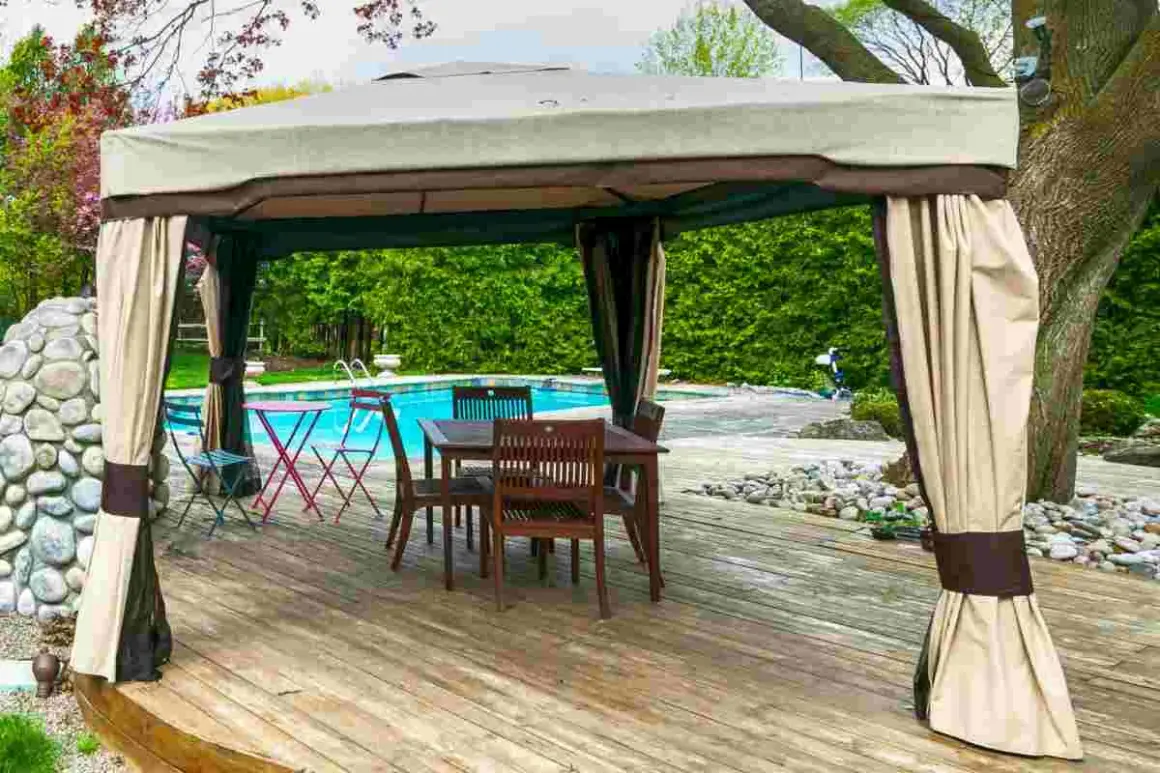 Gazebo su terrazza in legno, con tavolo e sedie, vicino a una piscina. Soluzione per come fissare un gazebo su terrazza senza bucare il pavimento.