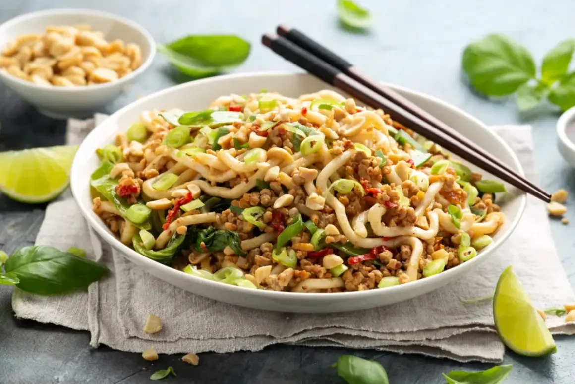Pyszne danie z makaronem, mielonym mięsem i zielonymi warzywami, inspirowane przepisami na kapustę pak choi. Posypane orzeszkami ziemnymi.