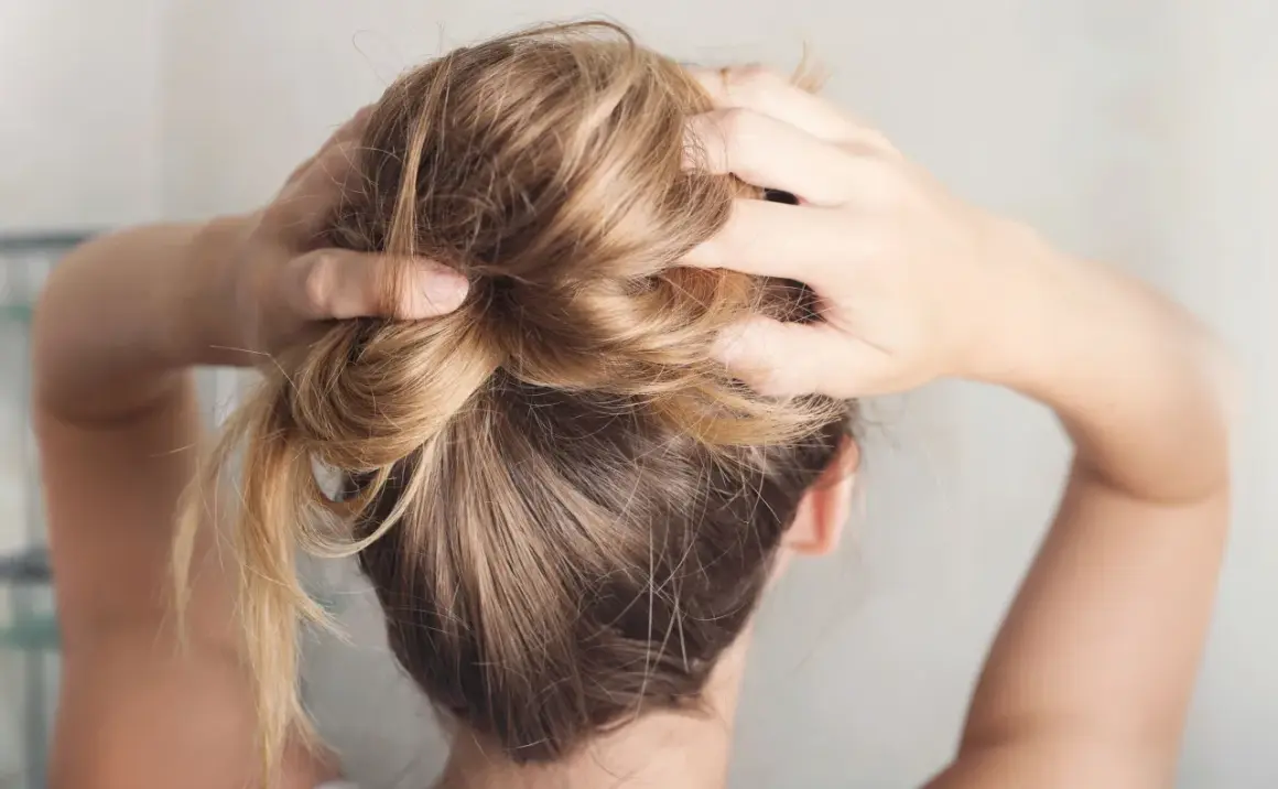 Hände formen einen unordentlichen Dutt, eine von vielen leichten Frisuren für den Alltag.