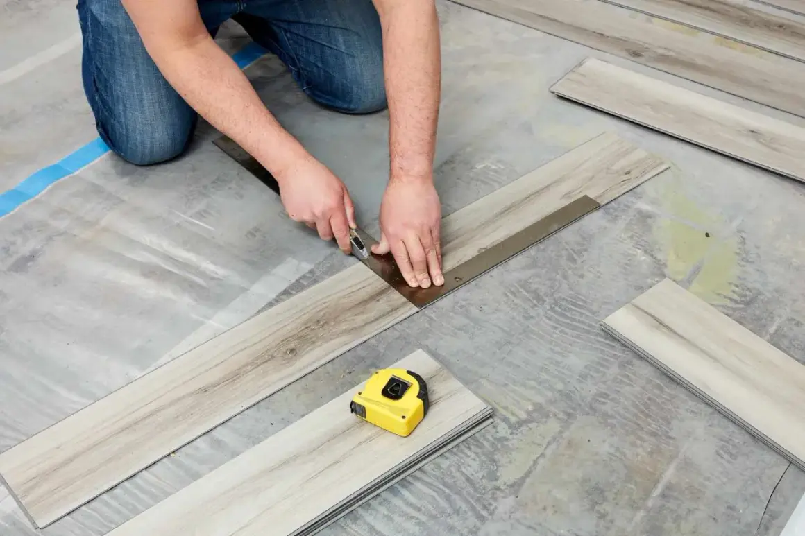 A person is cutting vinyl plank flooring that is not laying flat during installation. A tape measure is nearby.