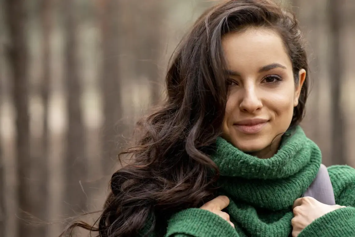 Brunetka w zielonym swetrze, idealne kolory dla brunetek. Jej ciemne włosy falują na wietrze, a uśmiech rozjaśnia twarz.