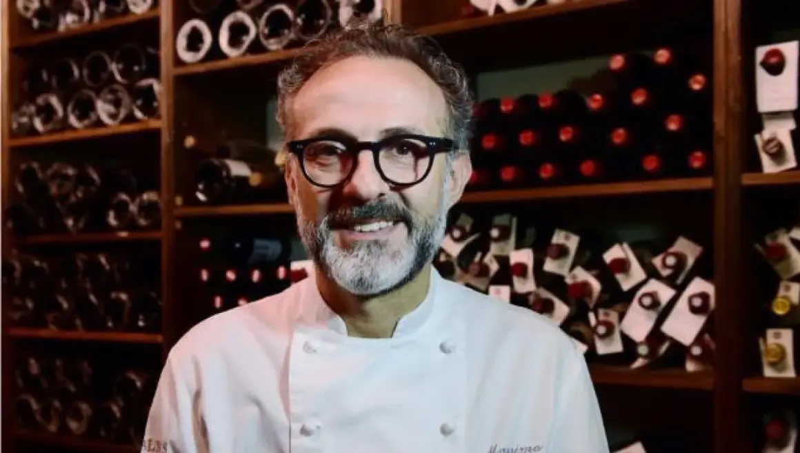 Un sorriso tra gli scaffali di bottiglie di vino, un ritratto di uno dei tanti chef stellati italiani che rendono la cucina italiana famosa nel mondo.