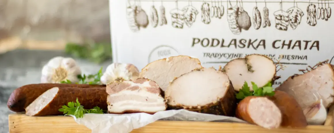 Swojskie wyroby wędliniarskie z Podlaskiej Chaty: kiełbasa, boczek, pieczone mięsa i czosnek. Tradycyjne smaki.