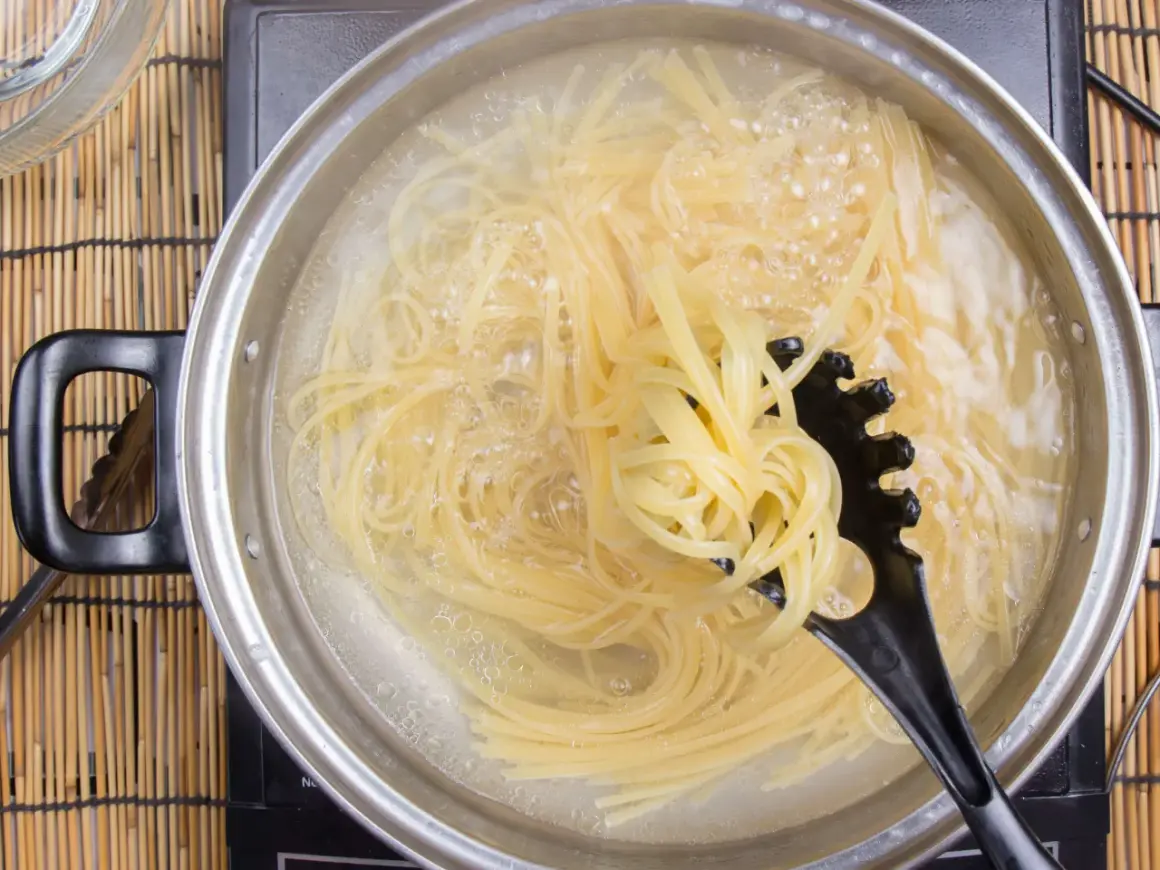 Spaghetti kochen in sprudelndem Wasser. Ein schwarzer Pastalöffel hebt eine Portion heraus, um zu zeigen, wie kleben spaghetti nach dem kochen nicht zusammen.
