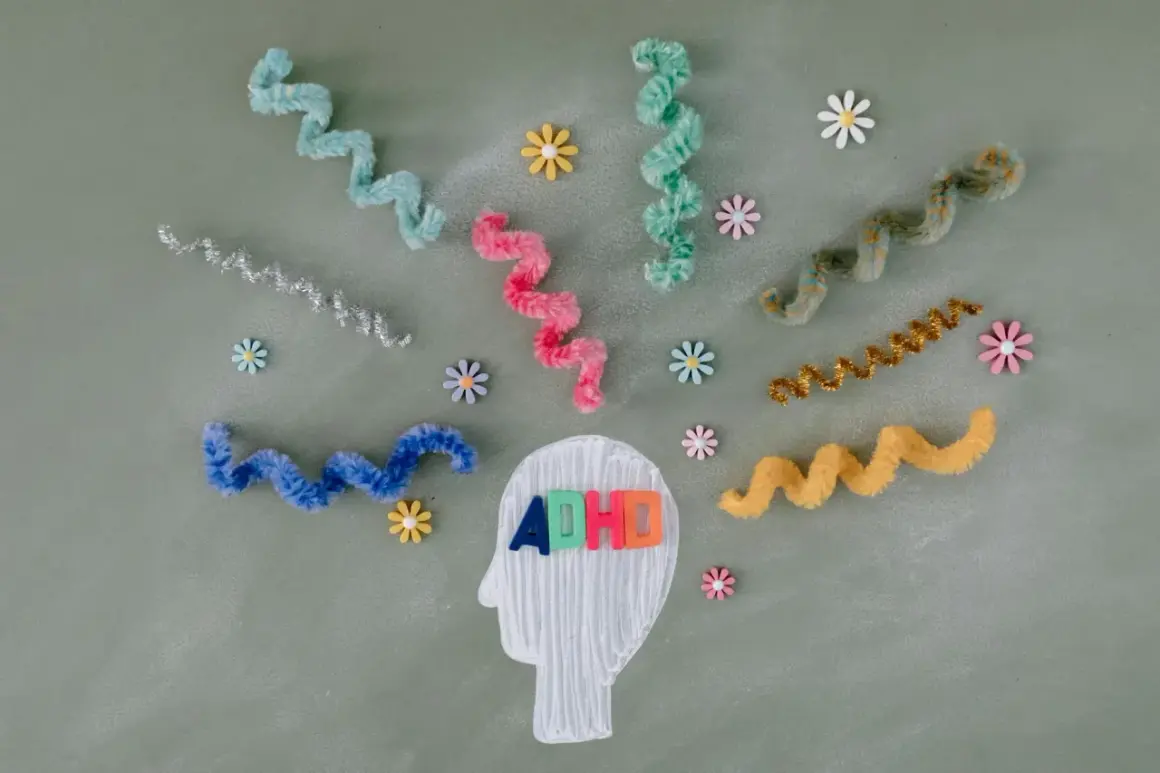 Kolorowe litery "ADHD" w głowie symbolizują diagnozę. Wirujące wstążki i kwiatki odzwierciedlają natłok myśli.