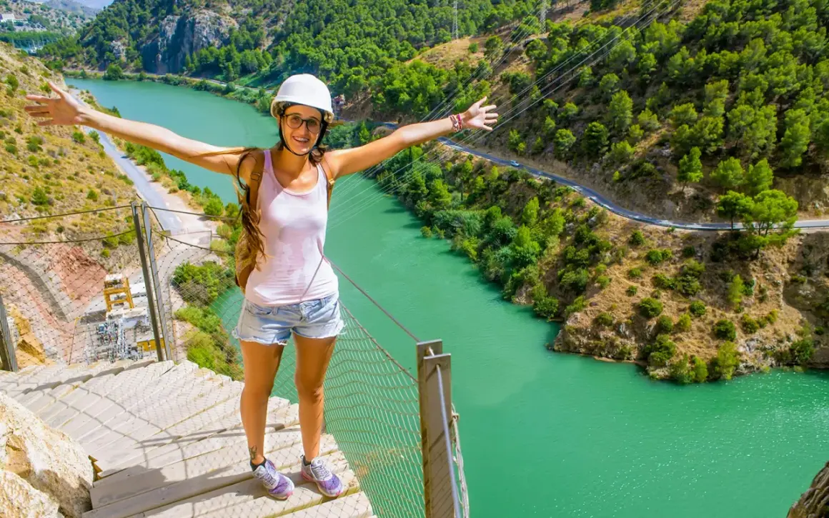 Glad kvinna med armarna utsträckta njuter av en fantastisk caminito del rey vandring med turkos flod nedanför.
