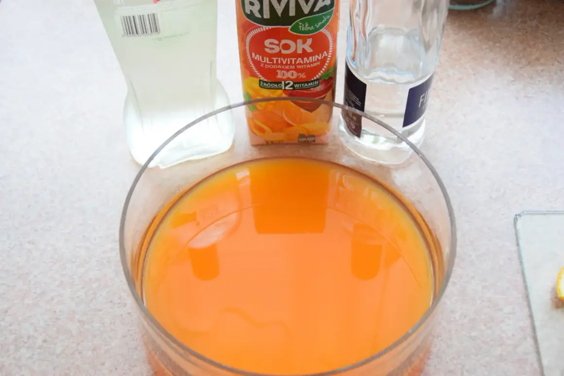 Pomarańczowy sok w dużej misie, obok karton soku multivitamin i butelka wody. Idealne składniki na orzeźwiający **jungle juice**.