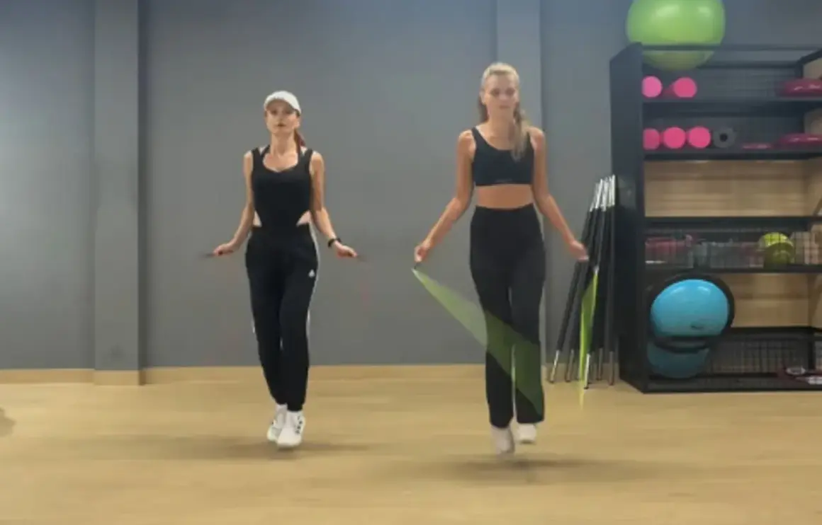 Dwie kobiety w strojach sportowych skaczą na skakance w sali gimnastycznej.