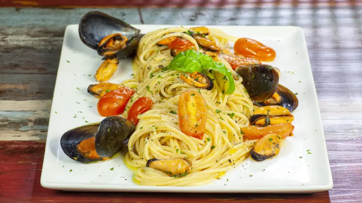 Un piatto invitante di spaghetti con le cozze e pomodorini, guarnito con basilico fresco.