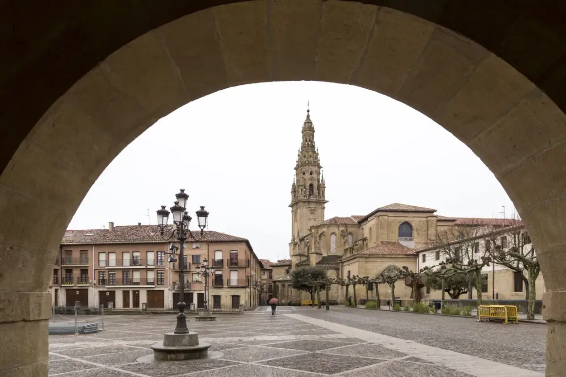 Plaza de Santo Domingo de la Calzada, con su imponente catedral y edificios históricos. Un peregrino con paraguas cruza la plaza empedrada.