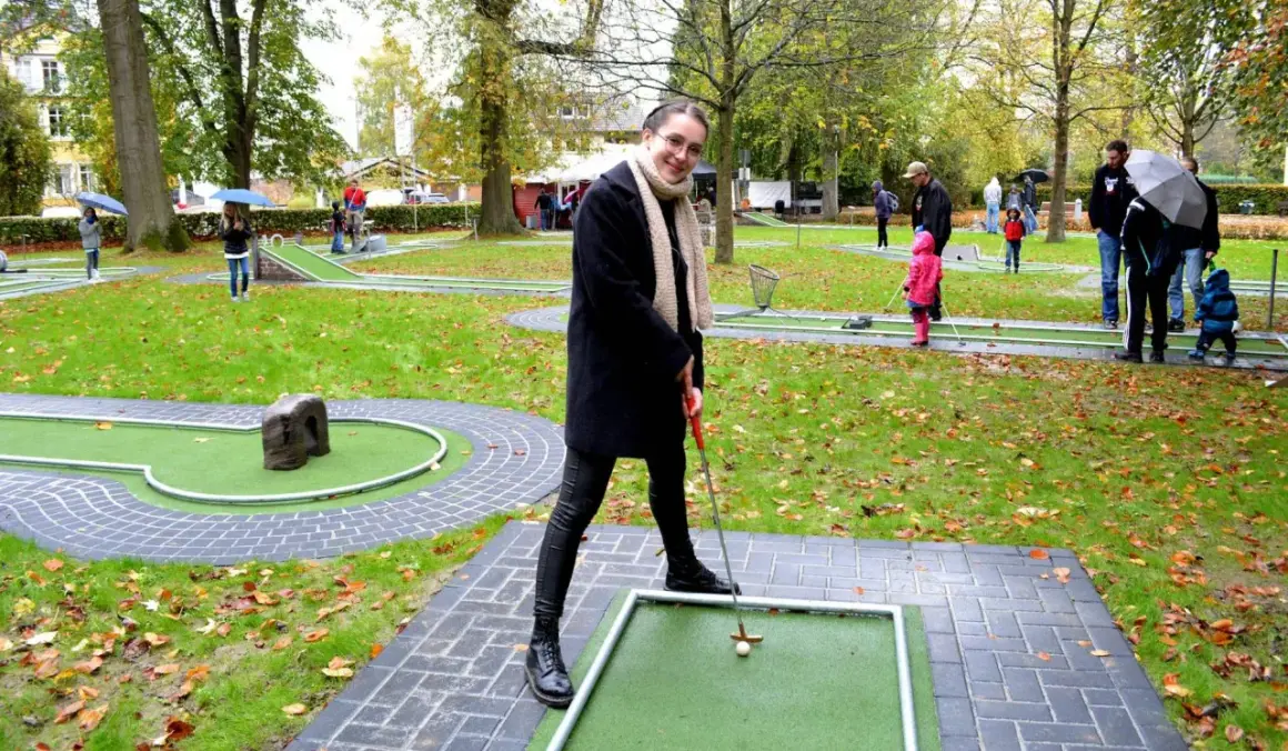 Frau spielt Minigolf in Hennef, im Hintergrund spielen weitere Personen.