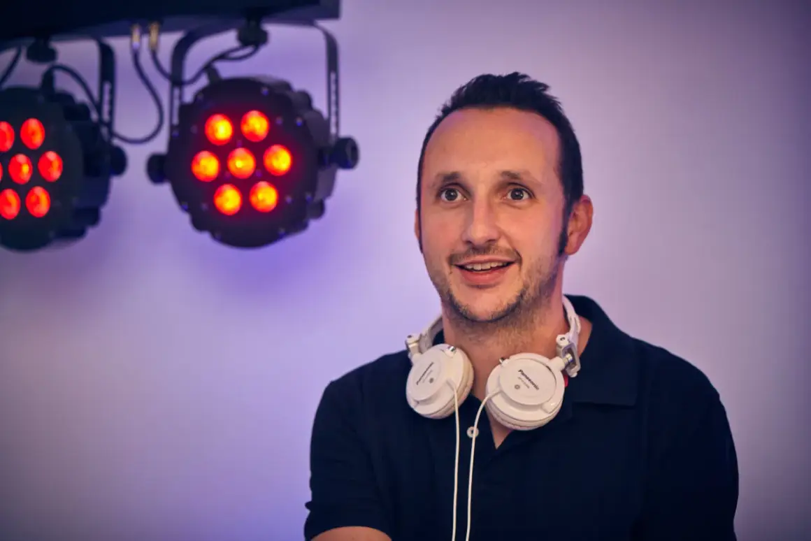 DJ mit Kopfhörern bereit für die Party in Bergisch Gladbach. Scheinwerfer leuchten im Hintergrund.