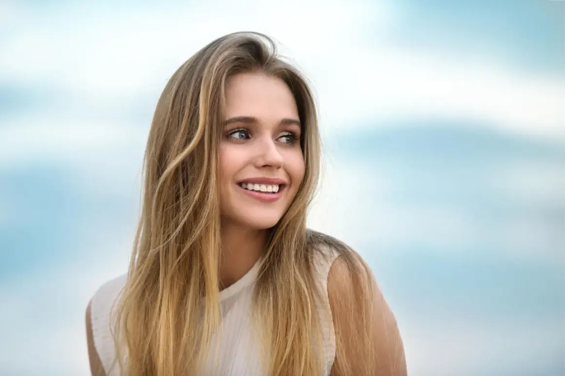 Lachendes junges Mädchen mit langen, welligen Haaren, die blonde Highlights auf dunkelblond zeigen.