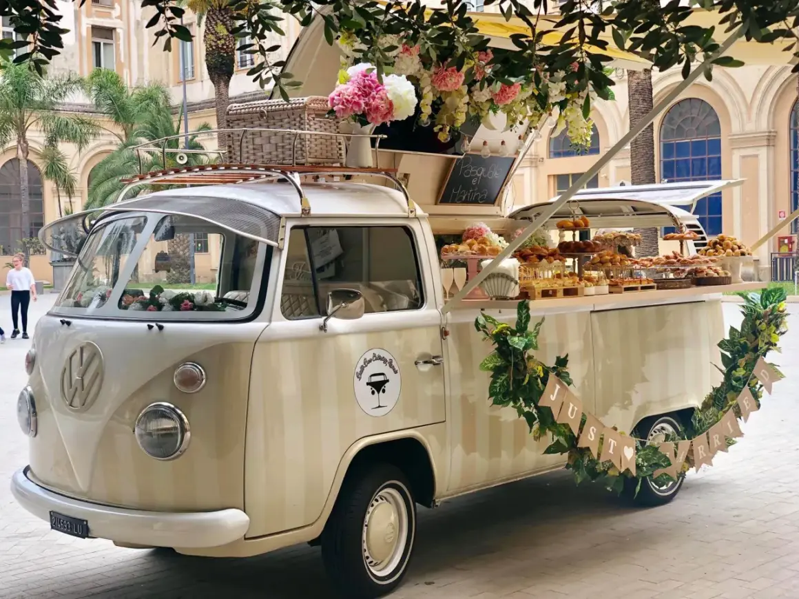 Un furgone vintage allestito per un aperitivo fuori chiesa matrimonio, con fiori e dolci.