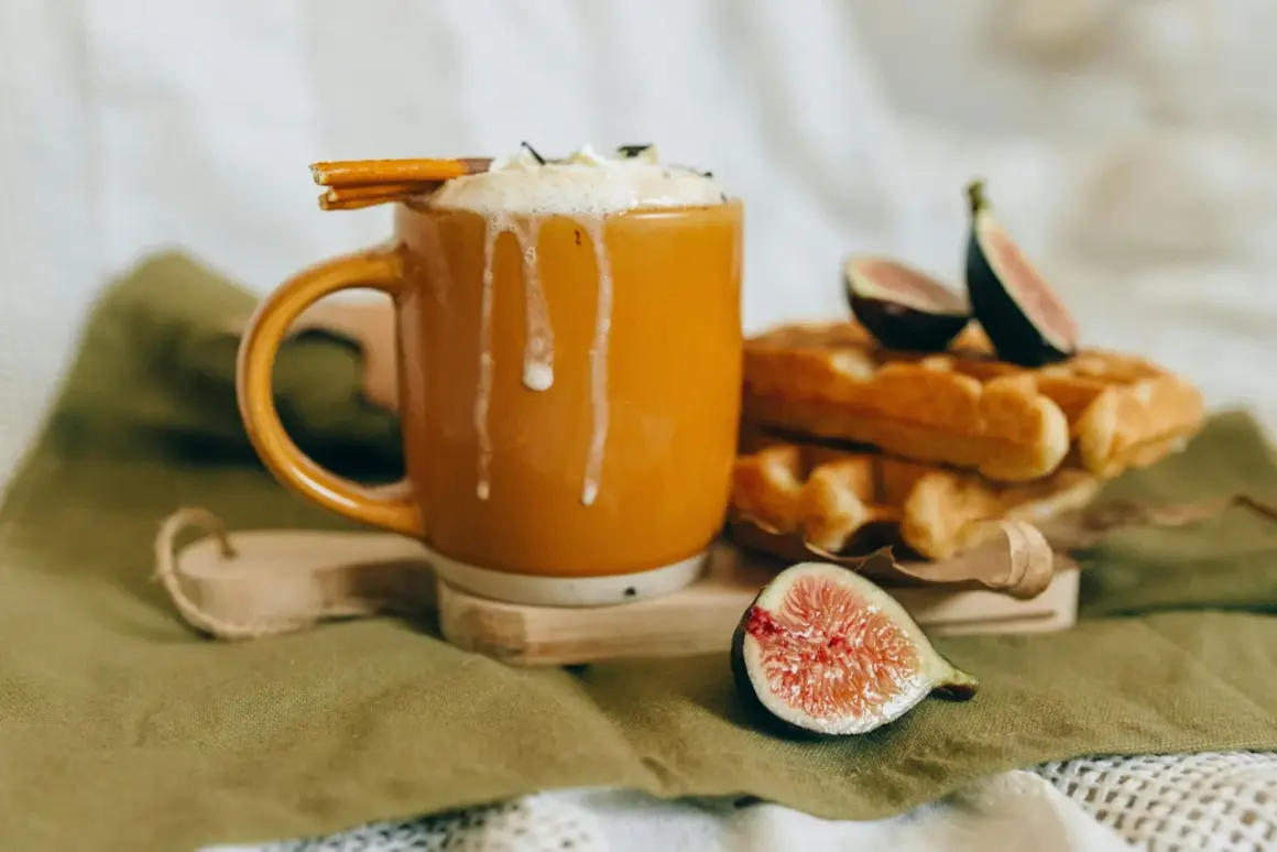En varm kopp chai latte med vispad grädde och kanelstång, bredvid nybakade våfflor och färska fikon. Perfekt för ett mysigt chai latte recept.