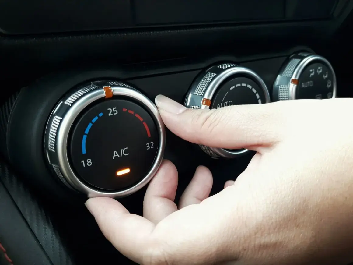 Dłoń reguluje pokrętłem temperaturę klimatyzacji w samochodzie, ustawiając ją na 25 stopni.