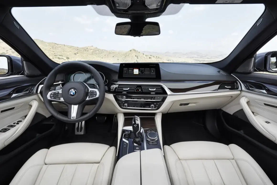 Wnętrze BMW 5 G30 z jasną tapicerką, drewnianymi wstawkami i nowoczesnym ekranem multimedialnym.