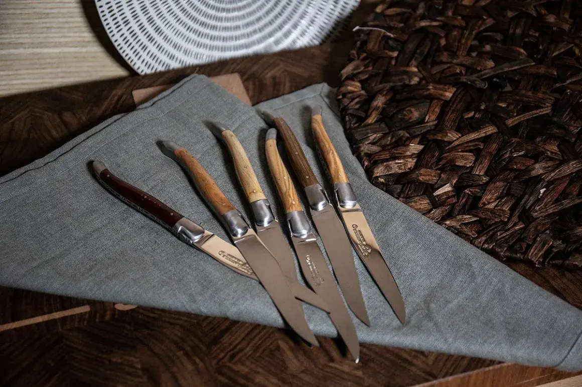 Cinco cuchillos de una prestigiosa marca de cuchillos, con mangos de madera y acero pulido, dispuestos sobre un paño gris.