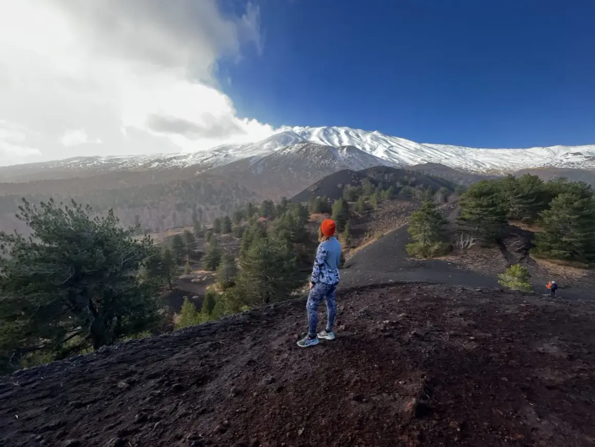 Kobieta w pomarańczowej czapce podziwia majestatyczny wulkan Etna pokryty śniegiem.