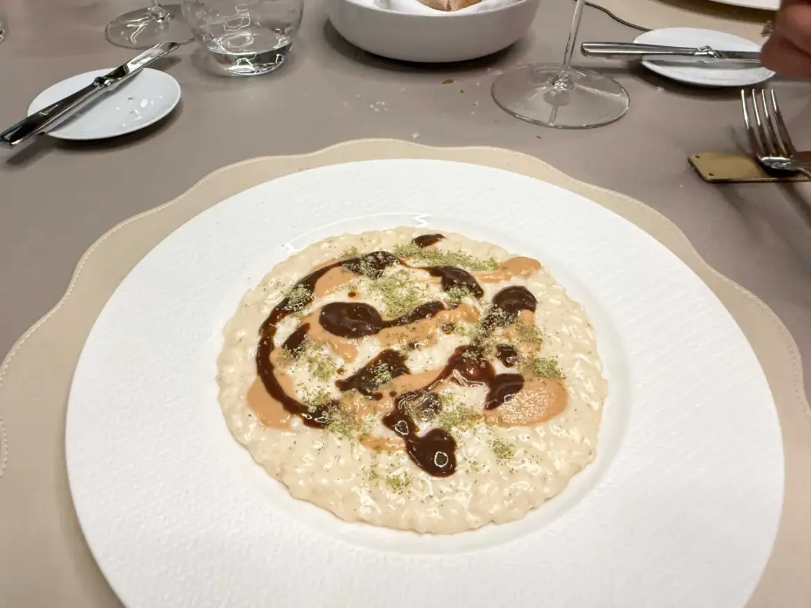 Un risotto cremoso con salse scure e chiare, guarnito con erbe verdi. Andrea la Rossa lo ha preparato con cura.
