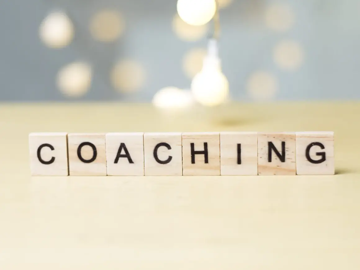Drewniane klocki z literami układają słowo "COACHING". To właśnie kim jest coach – osoba wspierająca rozwój.