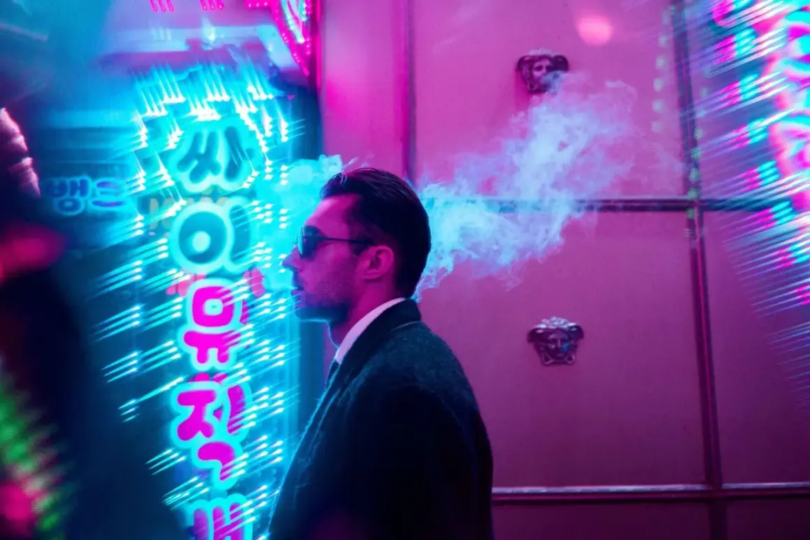 Man exhales smoke in front of vibrant neon signs, a cool example of led light photography ideas.