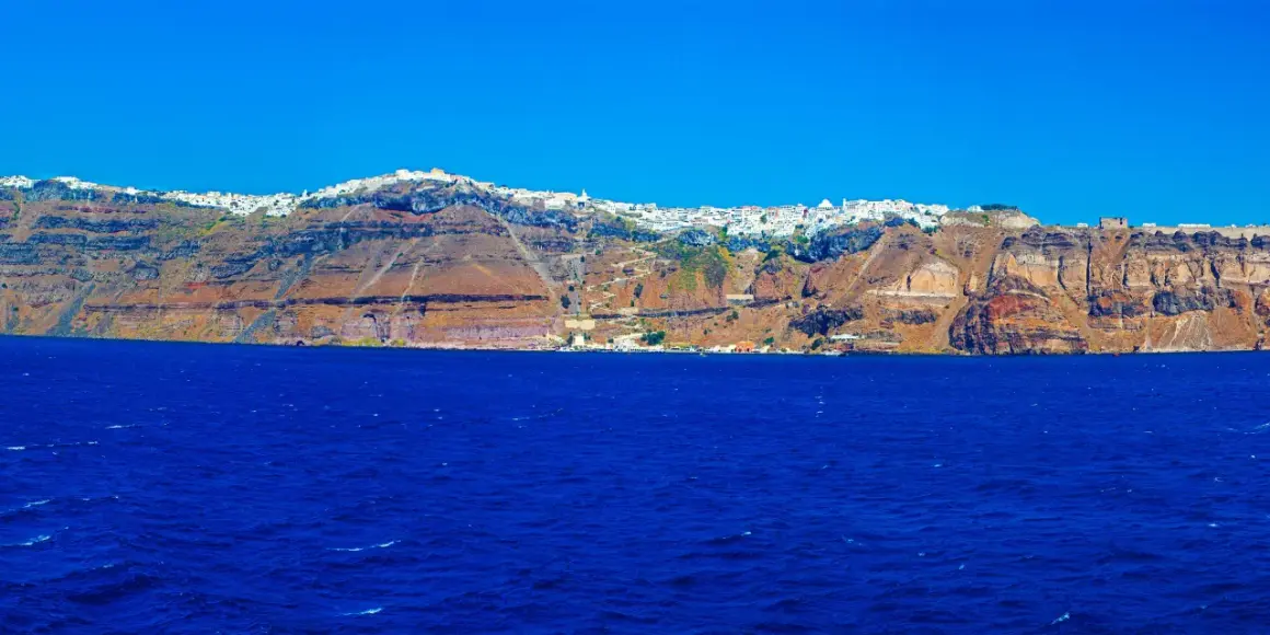 Widok na białe miasteczko na klifie nad błękitnym morzem na Santorini.