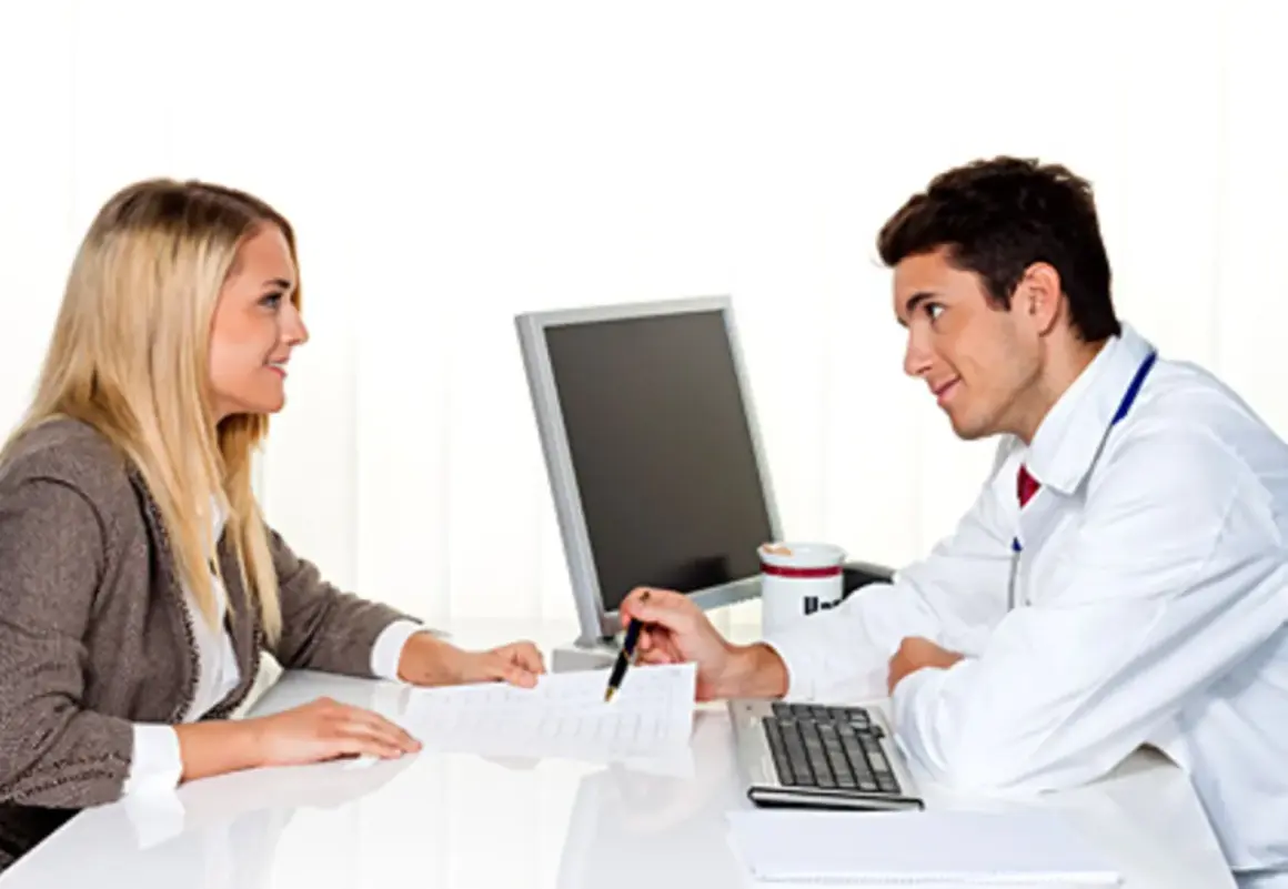 Arzt erklärt einer Frau, was passiert, wenn man die private Krankenversicherung nicht bezahlt. Sie besprechen Dokumente am Schreibtisch.
