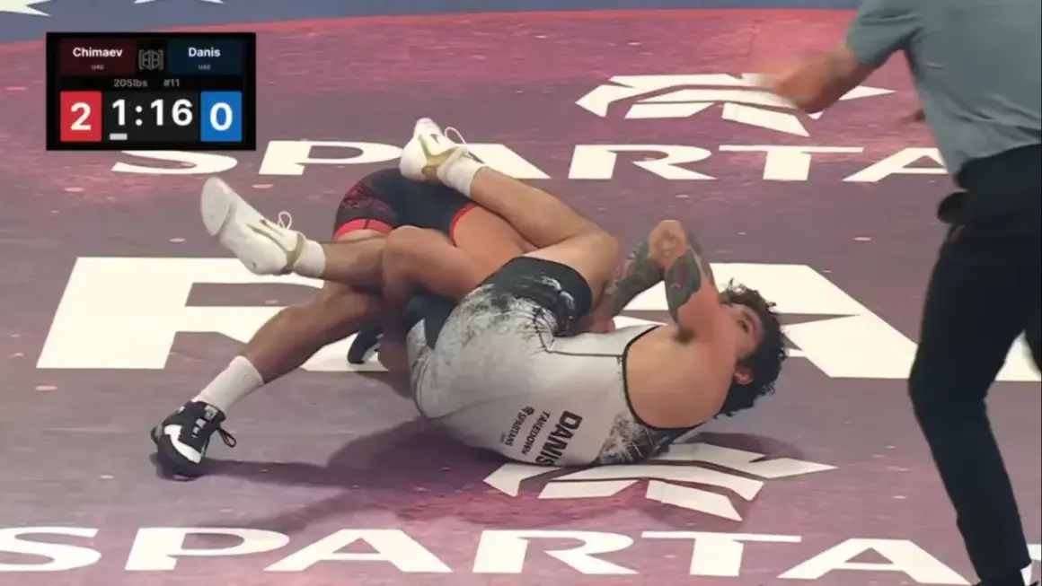 Intens kamp i catch wrestling. En brottare har den andra i ett grepp på mattan.
