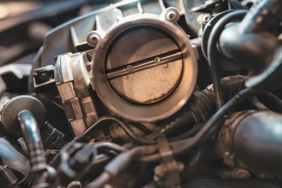 Gros plan sur un boîtier papillon reste ouvert sur un moteur diesel. La lumière éclaire la pièce métallique et les conduits environnants.