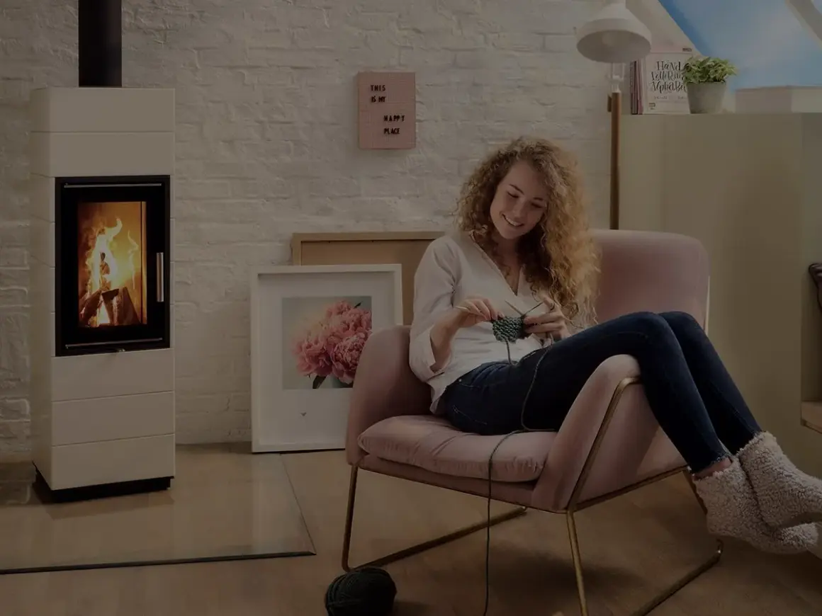 En kvinna stickar i en mysig fåtölj bredvid en modern gasol öppen spis.