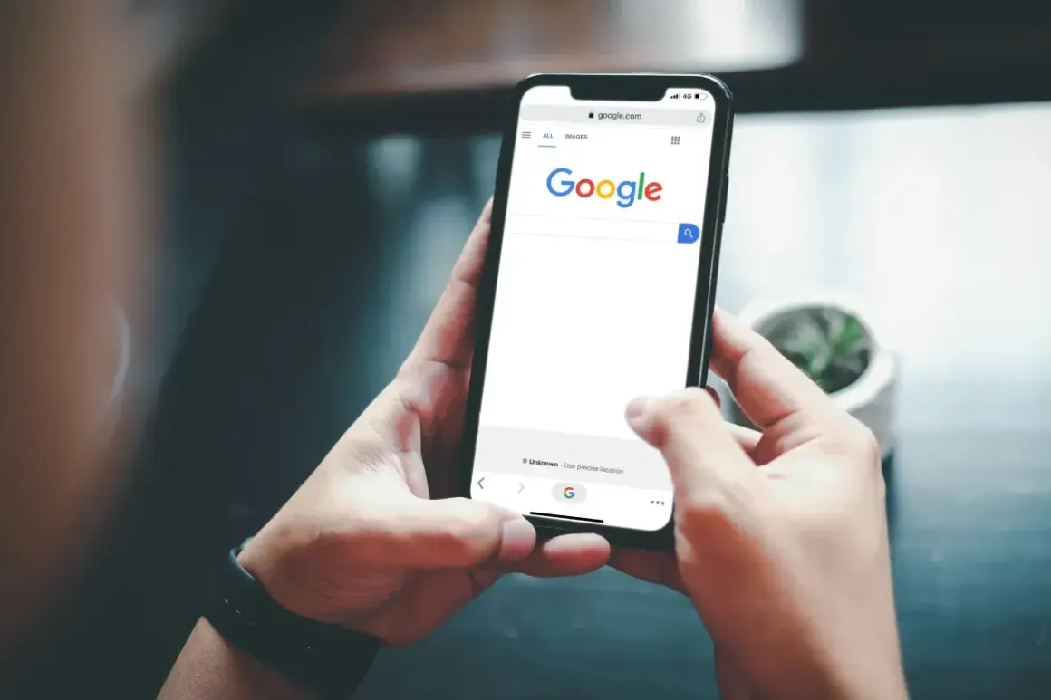 Dłonie trzymające smartfon z otwartą stroną Google.