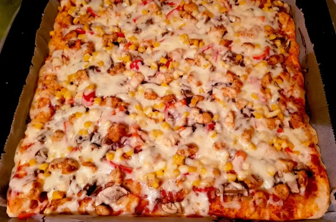 Pyszna pizza domowa na blachę z kurczakiem, kukurydzą i pieczarkami, obficie posypana serem. Idealna na rodzinny obiad.