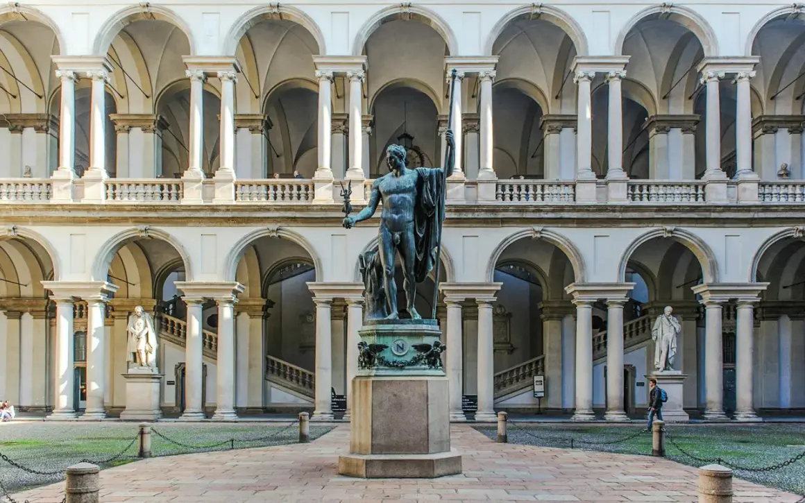 Dziedziniec Pinacoteca di Brera z rzeźbą w centrum i arkadowymi galeriami.