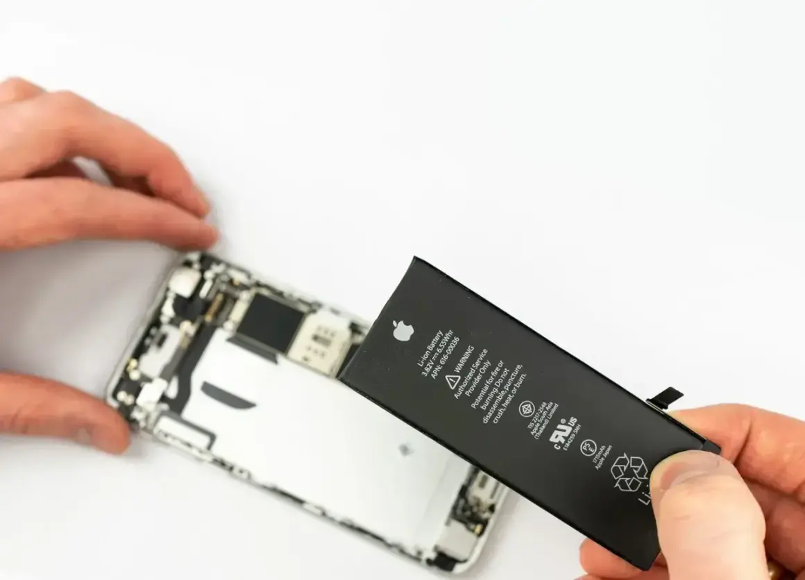 Wymiana iPhone jest potrzebna, gdy bateria jest zużyta. Dłoń trzyma nową baterię obok rozebranego telefonu.