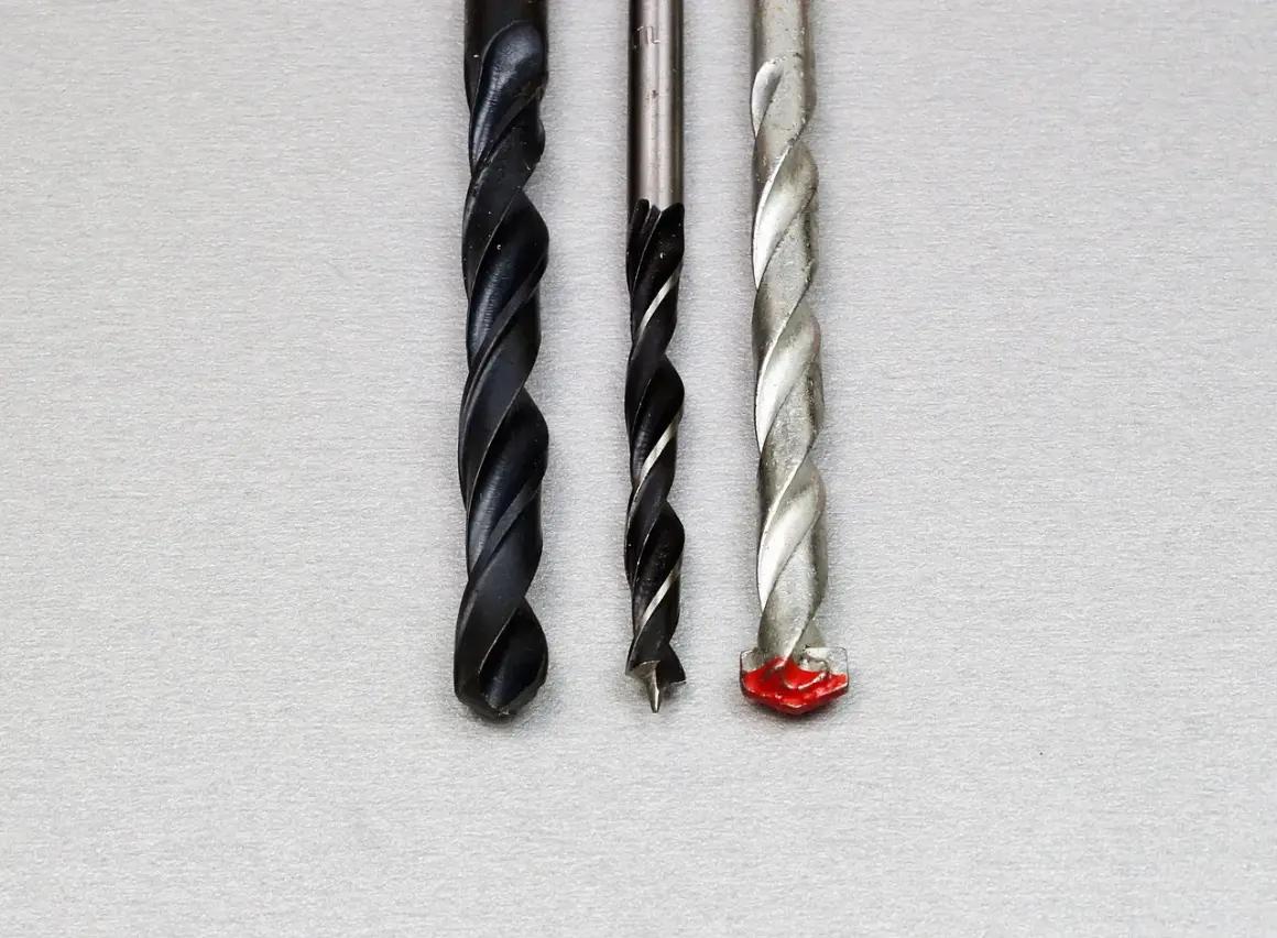 Trois forets de tailles différentes, dont un avec une pointe rouge, prêts à percer un chemin à travers un matériau, comme un foret dans un foret.