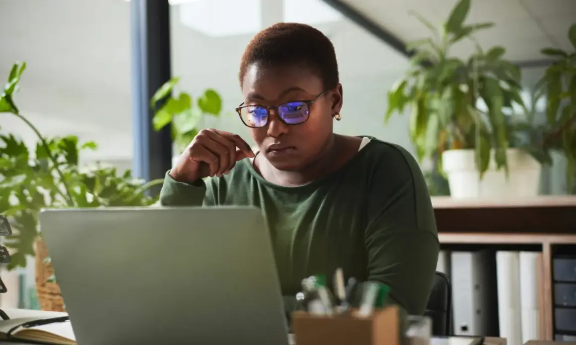 A woman with glasses intently studies her laptop, perhaps researching alternative investment partners for her next venture.