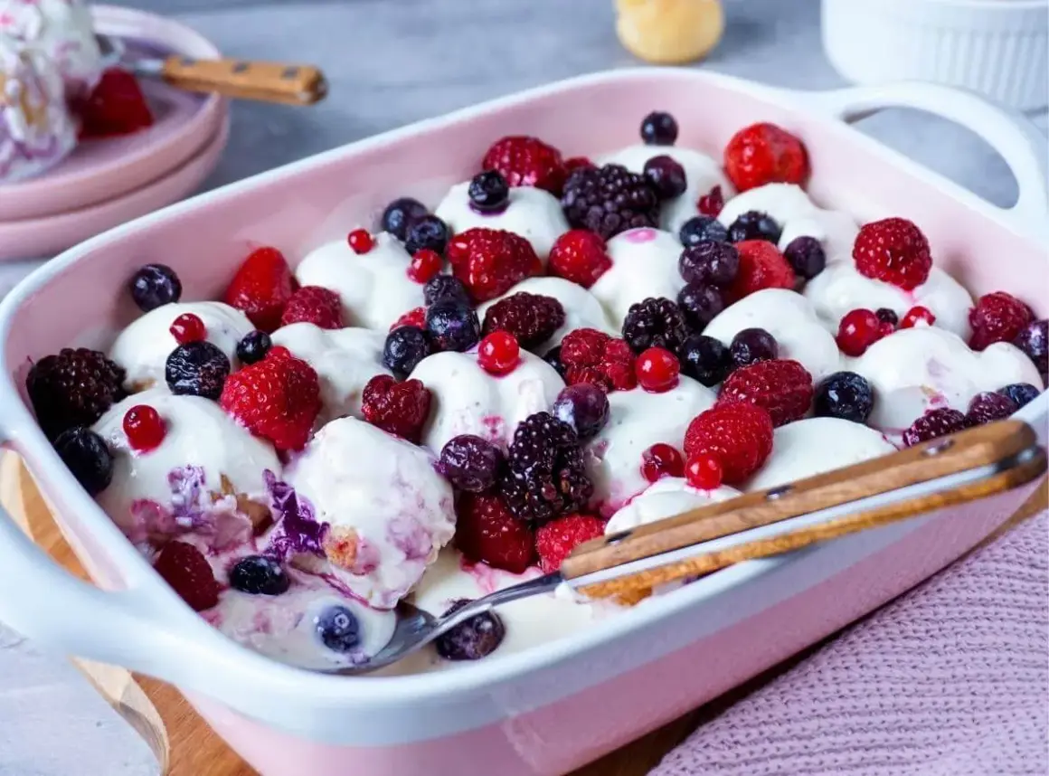 Ein cremiges Windbeutel-Dessert mit frischen Beeren wie Himbeeren, Blaubeeren und Brombeeren in einer rosa Schale.