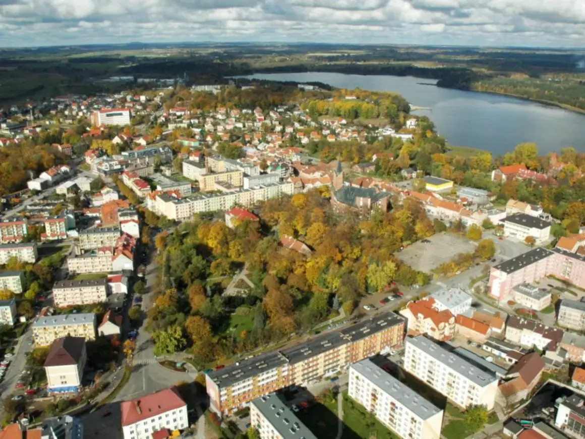 Widok z lotu ptaka na miasto z jeziorem w tle. Widać zabudowania, drzewa w jesiennych barwach i kościół. To największy rynek w Polsce.